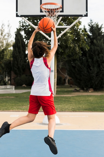 Foto completa da menina jogando na cesta de basquete