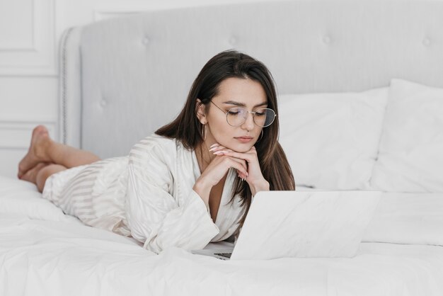 Foto completa de mulher trabalhando na cama com um laptop