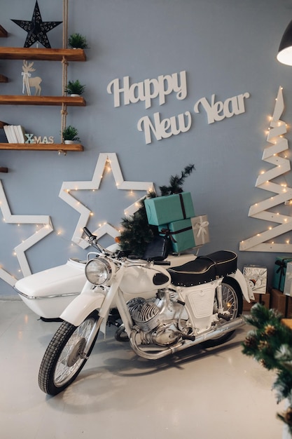 Foto conservada em estoque da motocicleta branca com árvore de Natal em miniatura e presentes de Natal embrulhados no berço. Interior atmosférico para o dia de Natal. Ano Novo de 2020.