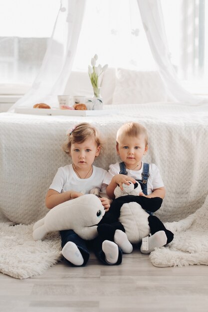 Foto conservada em estoque de duas lindas crianças sentadas no chão com dois brinquedos de pelúcia nas mãos