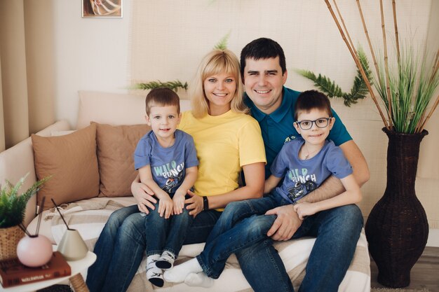 Foto conservada em estoque de uma linda família alegre com dois filhos em idade pré-escolar, sentados no sofá aconchegante e sorrindo para a câmera. Pai, mãe e dois filhos curtindo o tempo juntos.