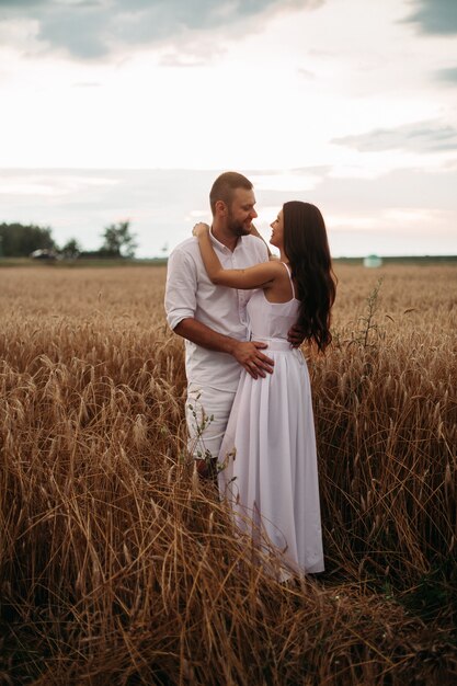 Foto conservada em estoque retrato de namorado barbudo abraçando sua linda namorada tanto em roupas brancas, abraçando no campo de trigo. Belo campo de trigo em segundo plano.