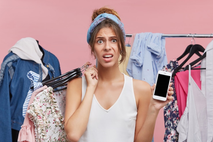 Foto grátis foto da bela jovem européia com aparência frustrada e preocupada, porque gastou todo o dinheiro com seu contador na compra de roupas novas, segurando hagers com roupas e telefone celular