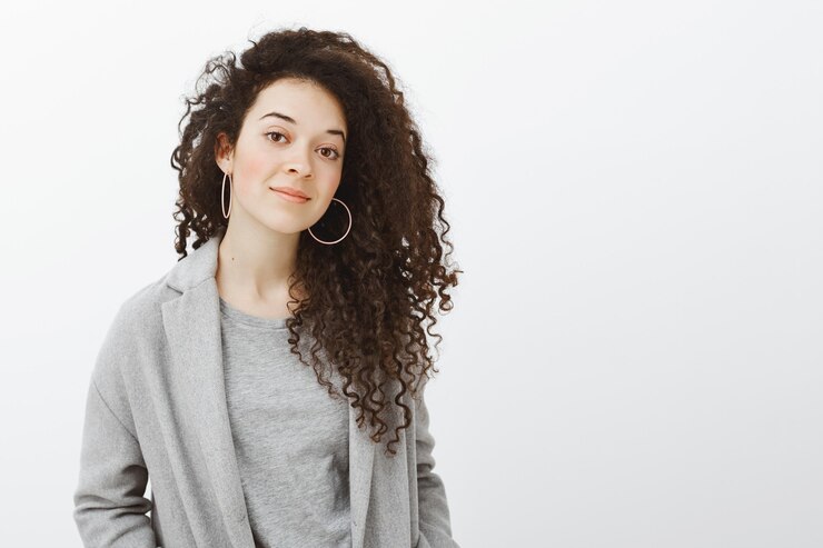 Foto grátis foto da cintura de uma mulher bonita e criativa com cabelo encaracolado em um casaco cinza e brincos, sorrindo amplamente e inclinando a cabeça, ouvindo com atenção enquanto trabalhava com colegas de trabalho