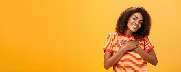 Foto da cintura para cima de uma encantadora mulher sensual de pele escura com penteado encaracolado em uma camiseta da moda segurando um amigo