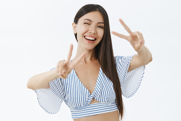 Foto da cintura para cima de uma mulher asiática encantadora, animada e emocionada, usando uma blusa curta mostrando paz