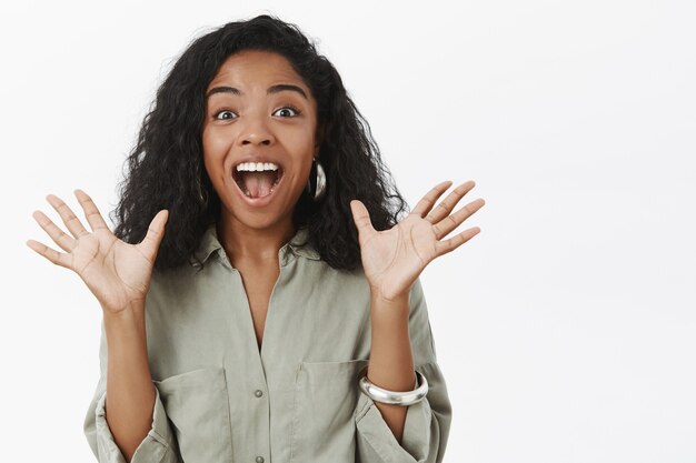 Foto da cintura para cima de uma mulher de pele escura encantadora e entusiasmada com um penteado encaracolado elegante levantando as palmas das mãos em emoção