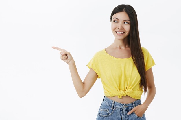 Foto da cintura para cima de uma mulher feminina encantadora, curiosa e emotiva, com cabelos longos e lisos em uma camiseta amarela cortada segurando a mão no bolso