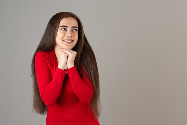 Foto da menina adorável sorridente em pé de moletom vermelho na parede cinza.