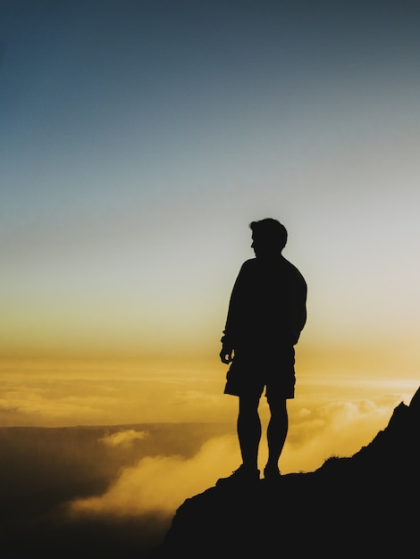 Foto da silhueta de um homem parado em um penhasco olhando o pôr do sol