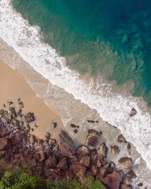 Foto da vista superior das ondas de espuma atingindo a costa rochosa da praia de Varkala