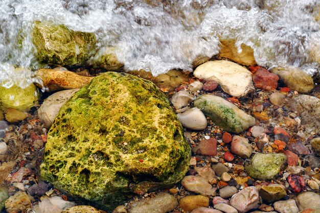 Foto da vista superior de uma grande rocha verde na praia ao lado de pequenas outras coloridas