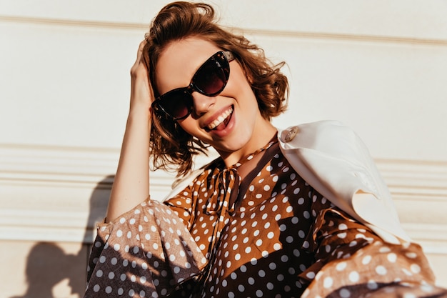 Foto de adorável mulher satisfeita em óculos de sol pretos. tiro ao ar livre de senhora encaracolada refinada expressando felicidade.