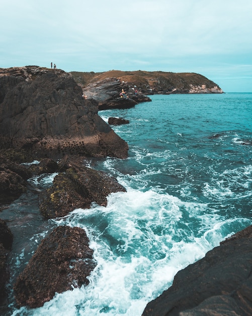 Foto de alto ângulo das ondas do mar batendo nas rochas com um céu nublado