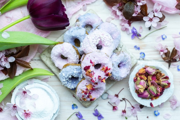 Foto de alto ângulo de alguns donuts veganos azuis e roxos cercados por flores em uma mesa