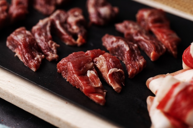 Foto de alto ângulo de pedaços de carne vermelha crua em uma placa preta sobre uma mesa de madeira