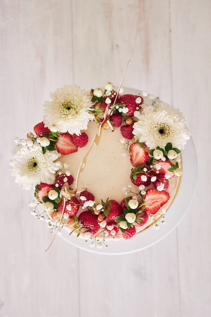 Foto de alto ângulo de um delicioso bolo de casamento branco com frutas vermelhas e flores na mesa de madeira branca