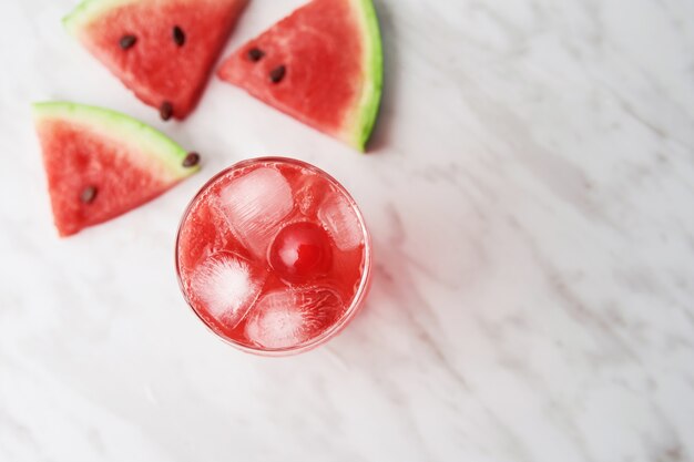 Foto de alto ângulo de uma bebida vermelha perto de fatias de melancia