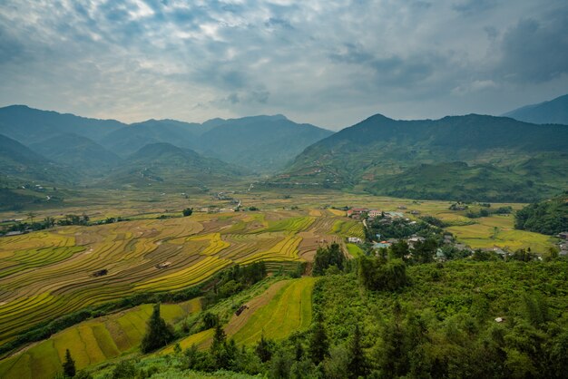 Foto de alto ângulo de uma bela paisagem verde com altas montanhas e casas sob as nuvens de tempestade