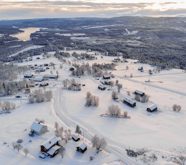 Foto de alto ângulo de uma cidade coberta de neve, rodeada por florestas e um lago sob um céu nublado