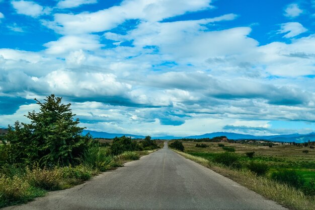 Foto de alto ângulo de uma estrada no vale sob o céu com grandes nuvens brancas