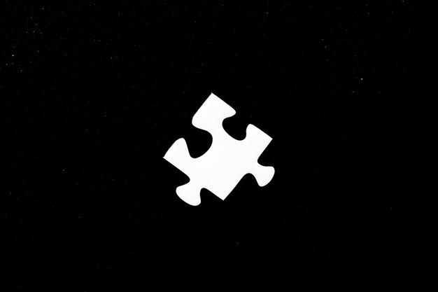 Foto de alto ângulo de uma peça branca de um quebra-cabeça em um fundo preto