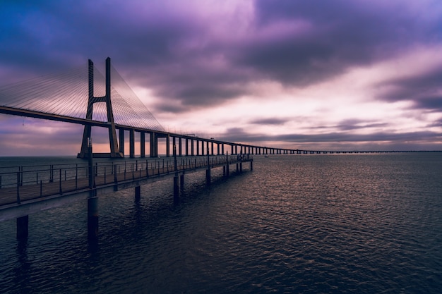 Foto de alto ângulo de uma ponte de madeira sobre o mar sob o céu roxo