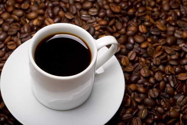 Foto de alto ângulo de uma xícara de café preto em uma superfície cheia de grãos de café