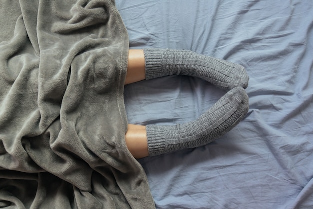 Foto de ângulo alto das pernas de uma mulher em meias de tricô cinza sob o cobertor
