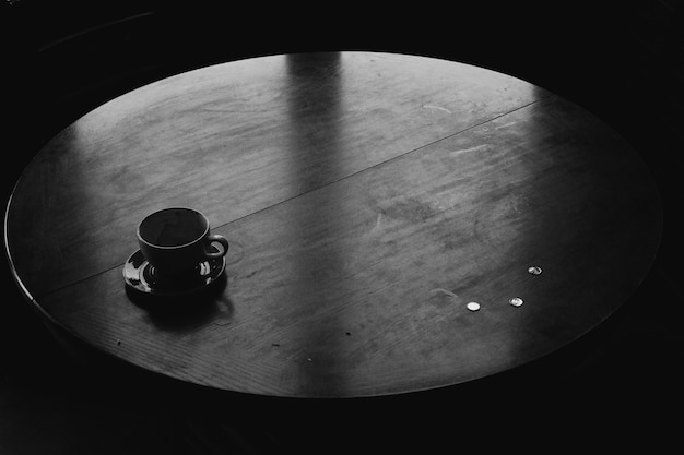 Foto de ângulo alto em tons de cinza de uma xícara de chá de cerâmica preta em uma mesa redonda de madeira