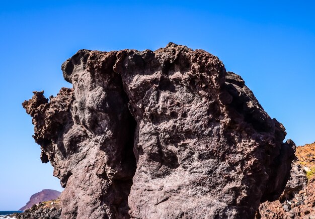 Foto de ângulo baixo de uma grande rocha em uma praia com céu azul claro