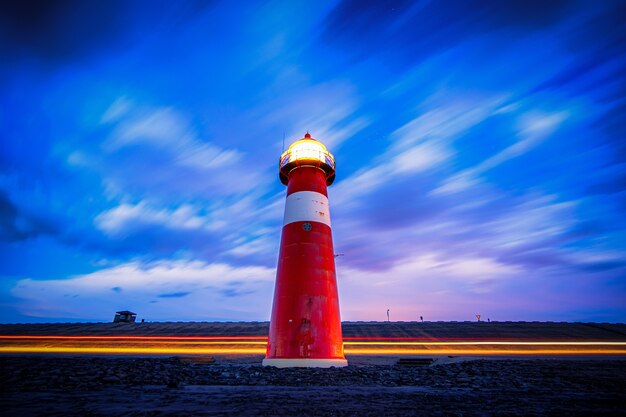 Foto de baixo ângulo de um farol aceso em vermelho e branco na estrada sob um céu nublado azul e roxo