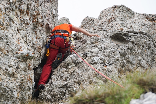 Foto de baixo ângulo de um homem escalando um penhasco rochoso em uma corda.