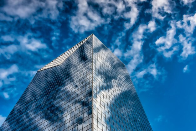 Foto de baixo ângulo de um prédio alto de vidro sob um céu azul nublado