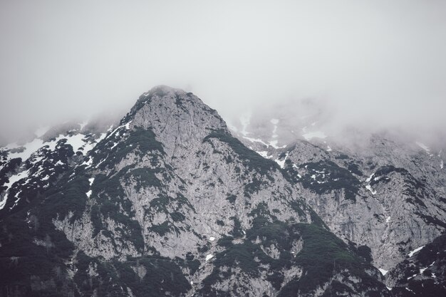 Foto de baixo ângulo de uma alta montanha rochosa coberta por uma névoa espessa