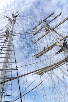 Foto de baixo ângulo dos mastros, cordames e cordas de um grande navio à vela sob um céu nublado