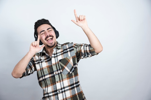 Foto de cara bonito em fones de ouvido, ouvindo uma música na parede branca.