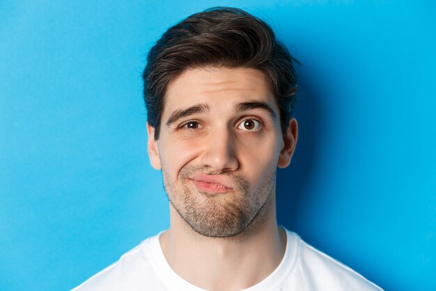 Foto de cara cético olhando para algo sem graça, fazendo careta e relutante em pé contra um fundo azul