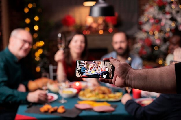 Foto de celebração de natal em família na tela do smartphone, foco seletivo, pessoas olhando para a câmera do celular, fundo desfocado. Férias de Natal, amigos reunidos