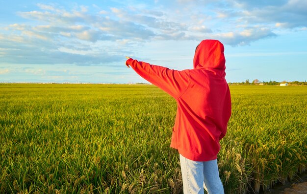 Foto de close de uma jovem vestida de vermelho, alegremente em pé em um campo verde em um dia ensolarado