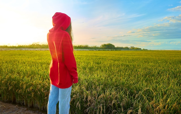 Foto de close de uma jovem vestida de vermelho, alegremente em pé em um campo verde em um dia ensolarado