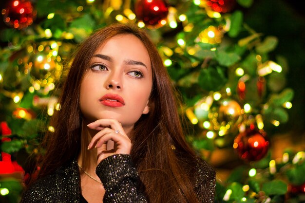 Foto de close de uma linda jovem em frente a uma árvore de Natal