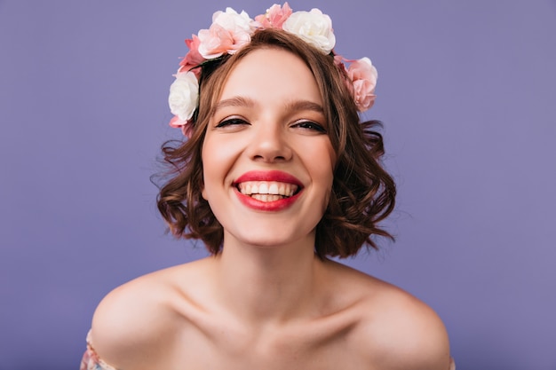 Foto de close-up de alegre menina branca com flores cor de rosa no cabelo. Mulher caucasiana emocional sorrindo.