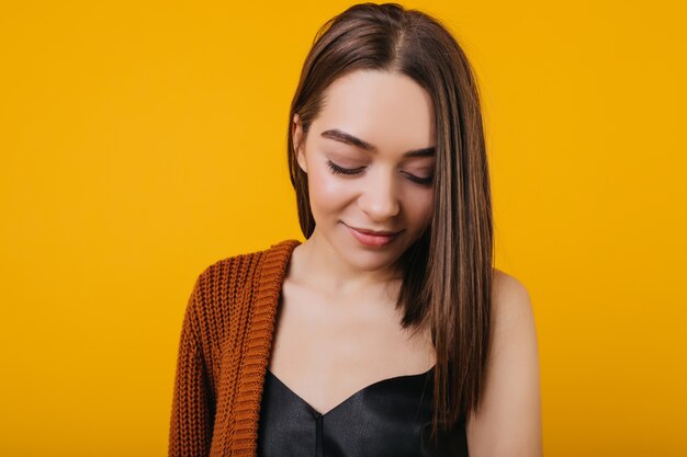 Foto de close-up de glamorosa garota de cabelos escuros posando com um sorriso tímido. Retrato de uma modelo feminino deslumbrante com penteado reto.