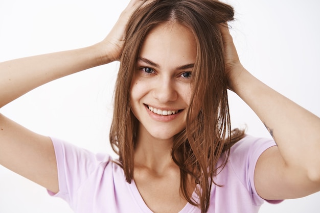 Foto de close-up de mulher bonita, confiante e feminina, tocando o corte de cabelo e sorrindo alegremente, sentindo-se bem para se livrar da acne sobre a parede cinza