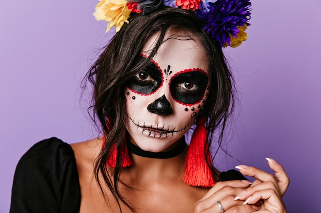 Foto de close-up de mulher vampiro usa guirlanda de flores coloridas. Menina caucasiana inspirada posando em traje de baile.