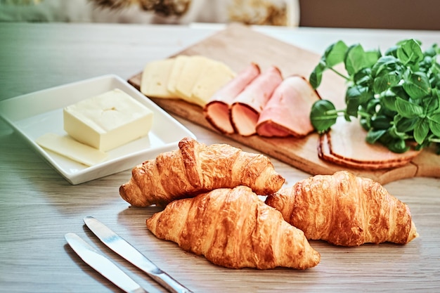 Foto de close-up de um croissant com presunto queijo e manteiga na placa de madeira em uma cozinha.