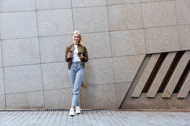 Foto de corpo inteiro de jovem com xícara de café e smartphone