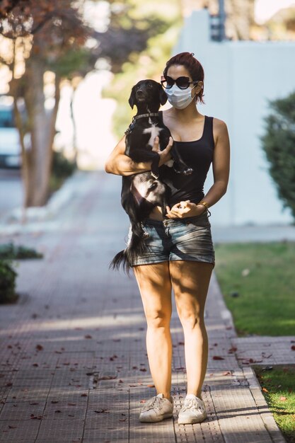 Foto de corpo inteiro de uma mulher com uma máscara segurando um cachorrinho fofo