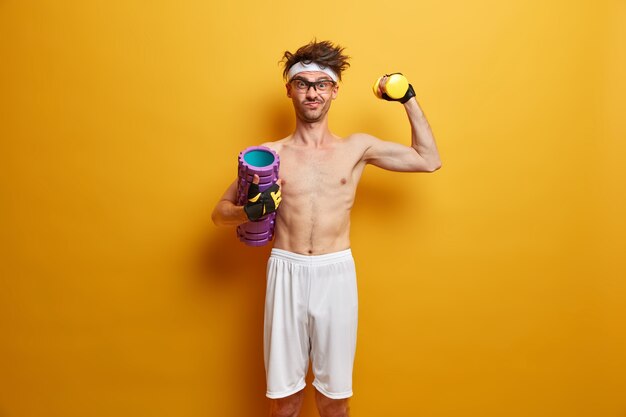 Foto de determinado homem atlético levanta halteres, posa com rolo de espuma, tem como objetivo ser forte, gosta de exercícios no ginásio, isolado na parede amarela. Conceito de pessoas, saúde e fitness. Estilo de vida saudável